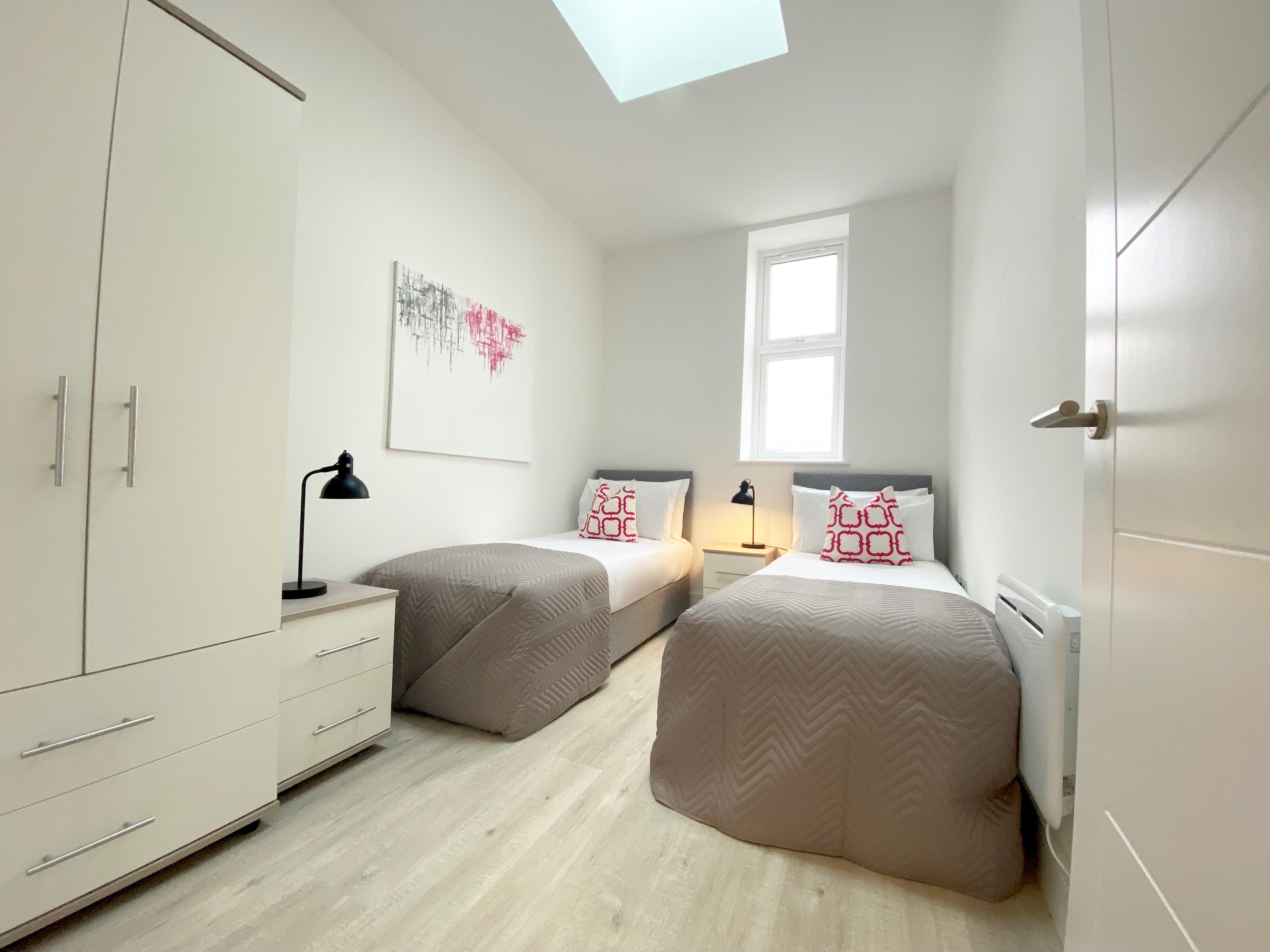 Two single beds with pink cushions, white wardrobe, white bedside