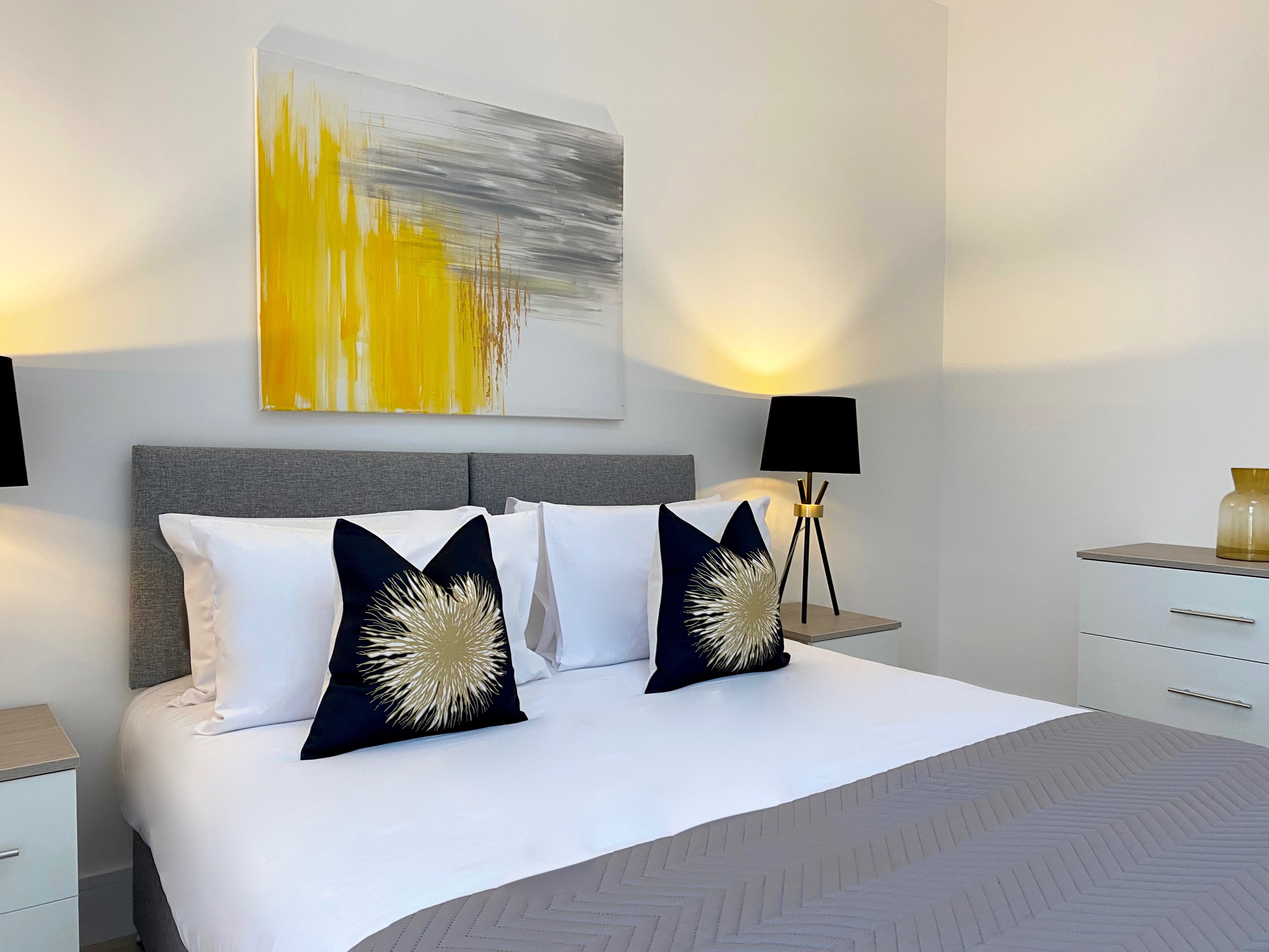 Bed with black and yellow cushions, bright yellow artwork and black lamps