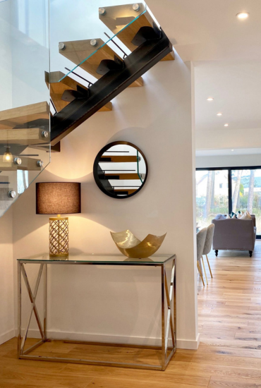 Wooden staircase with glass bannister, glass and silver console table, black table lamp and mirror