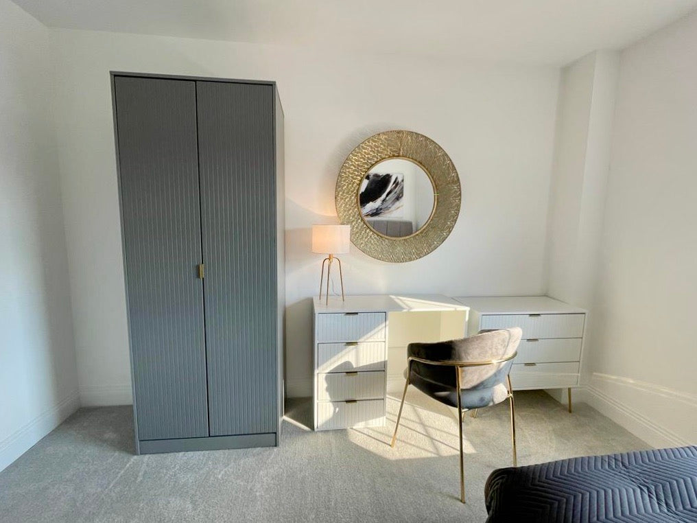 White desk, grey wardrobe, large gold mirror and grey velvet chair